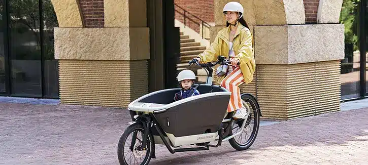Mujer circulando en una bicicleta de carga Urban Arrow con un niño por la ciudad